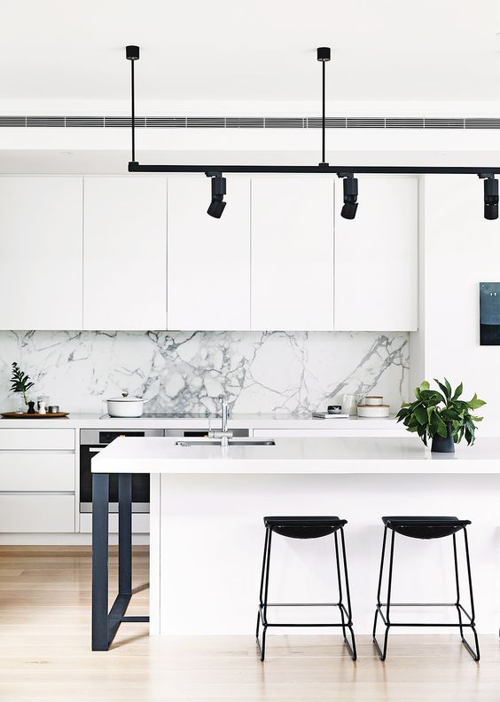 a modern white kitchen with a marble backsplash, black stools, lamps and legs