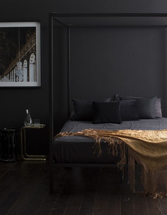 a moody bedroom with a framed black bed, black walls, bedding and some gold and brass touches here and there