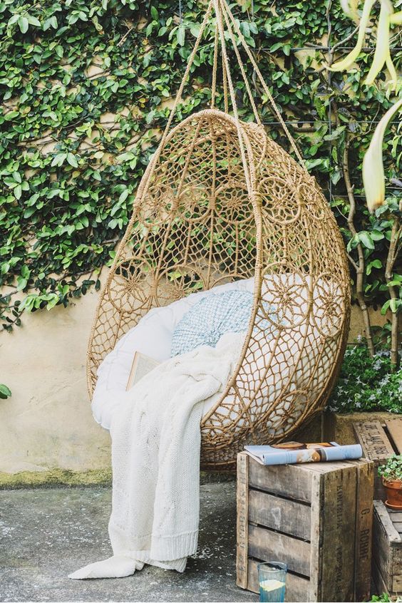 A boho inspired hanging chair with pillows and a blanket in the patio