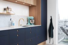 26 a modern cool kitchen in navy and wood with round holes as handles, a marble counterop and backsplash