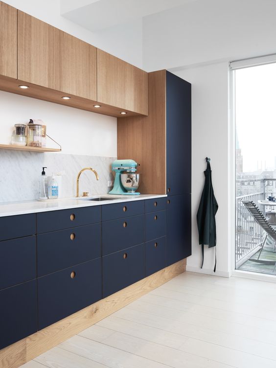 a modern cool kitchen in navy and wood with round holes as handles, a marble counterop and backsplash