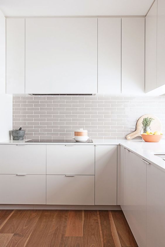 A modern white space is made more eye catchy with a grey tile backsplash and wooden floors