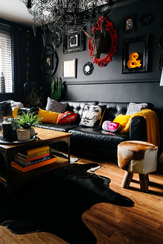 An eclectic space with black walls and furniture, a unique chandelier, framed artworks and clorful touches