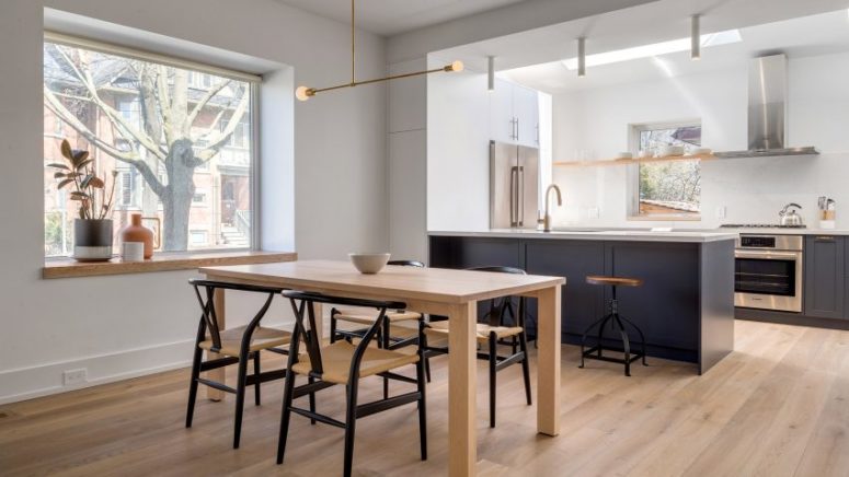 The dining room and kitchen are united, they are filled with natural light, with wishbone chairs and dark grey kitchen cabinets with white countertops