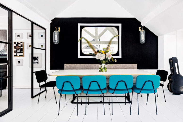 The dining space is done with a black accent wall, cool wall lamps and bold turquoise chairs