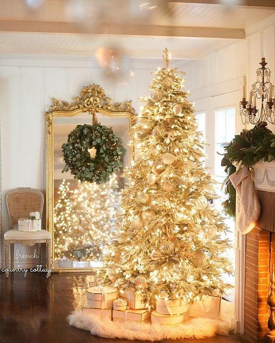 A gold pre lit Christmas tree with white ornaments and a faux fur skirt