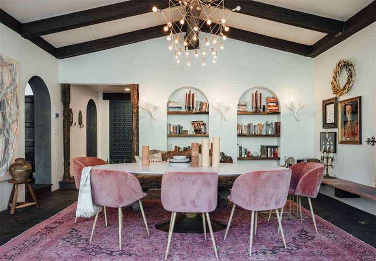 The dining space is done with black ceiling beams, dusty pink chairs and buil-in bookshelves that remind of castles