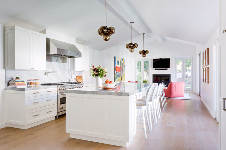 The kitchen is airy and light-colored, there's a sitting space with coral chairs and a built-in fireplace