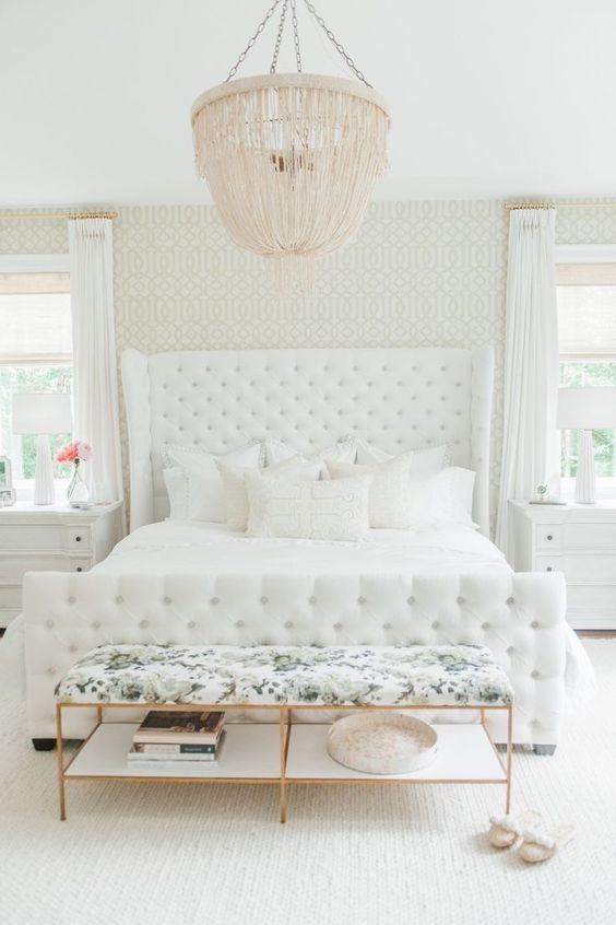 a creamy bedroom with a blush chandelier and a floral print upholstered bench
