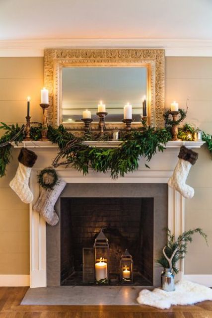 a lush greenery garland, candles and stockings plus candle lanterns inside a non-working fireplace