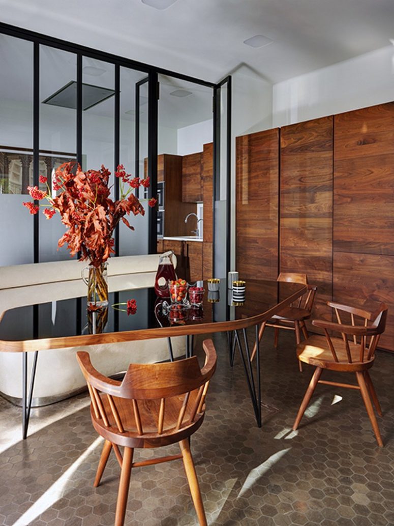 The dining space is done with a rich-colored wood cupboard, chairs and a chic table with a black glass top