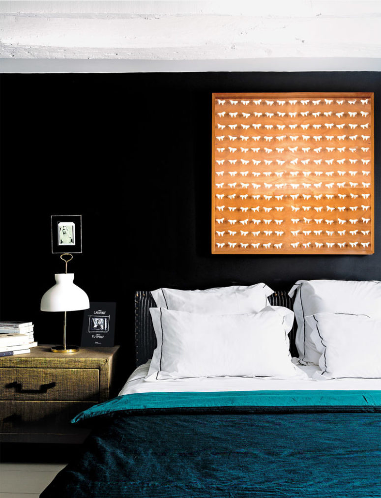 The master bedroom is done with a turquoise bedspread, with an orange artwork and a fabric covered nightstand