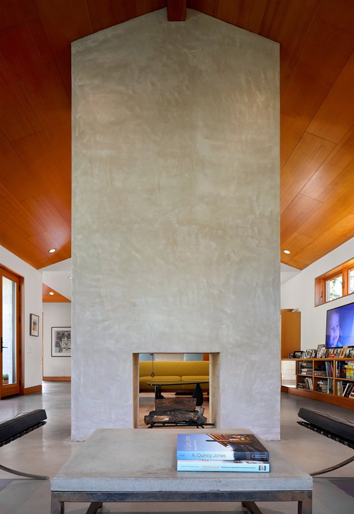 The fireplace with a concrete wall up to the roof is seen from all the sides and there's a matching coffee table