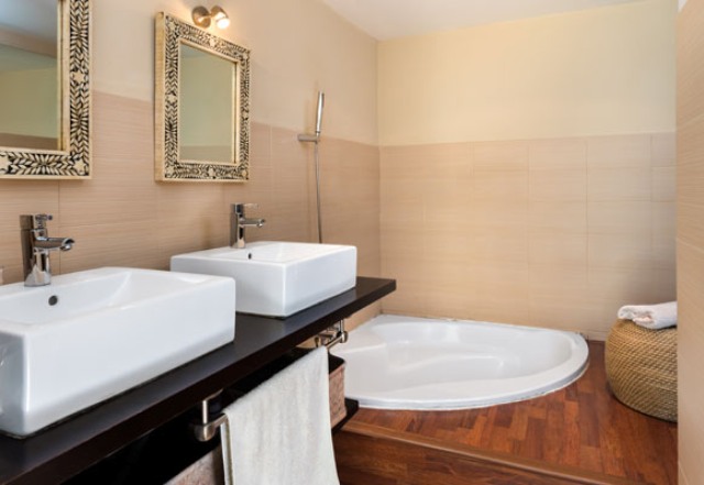 One of the bathroom features a sunken bathtub, a double vanity with sinks and a jute ottoman