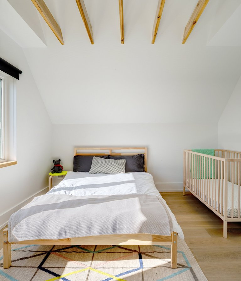 The bedroom features a bed, a colorful geo rug and a baby's crib