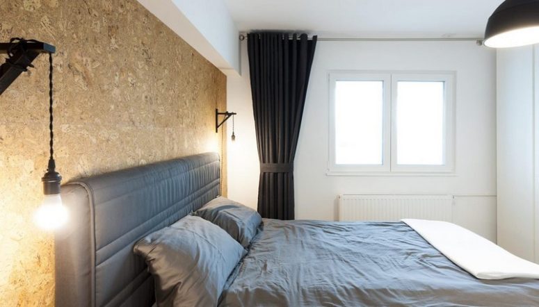 The bedroom features a cork wall, an upholstered bed, a black curtain