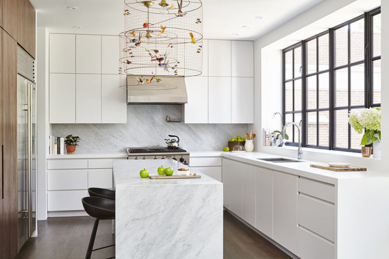The kitchen is done with sleek white cabinets, a wooden wall with built-in appliances and marble countertops