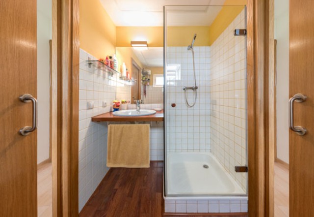 Another bathroom features a shower and a sink, the space is done with white tiles and natural wood