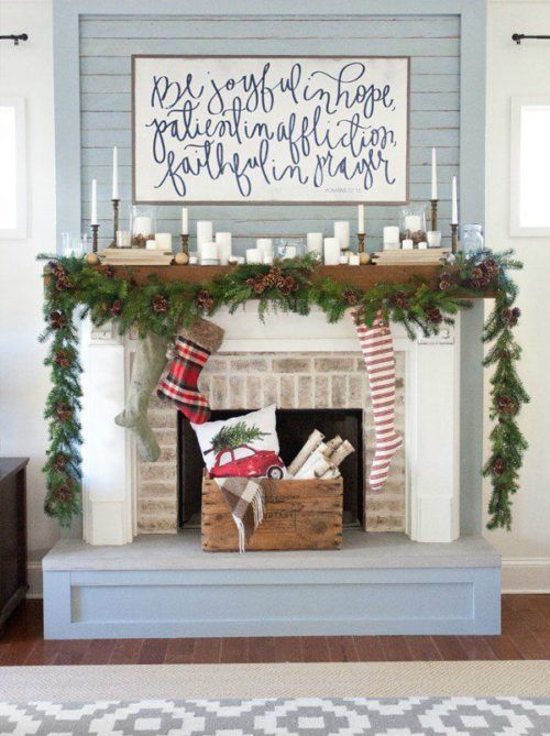 a rustic mantel with an evergreen and pinecone garland, candles and a sign over it