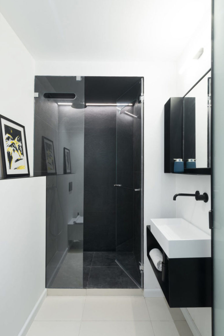 The bathroom is small, with a black tiled shower, all the rest is done in white
