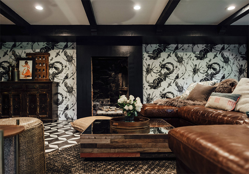 The living room is black and white, with eye catchy wallpaper, mosaic floors and brown leather furniture