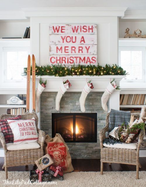 a whitewahsed pallet sign, a lush evergreen garland with lights, stockings and skis next to the fireplace