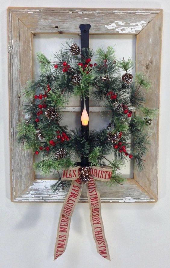 a window frame wreath of faux evergreens, berries and pinecones with a burlap bow and a light