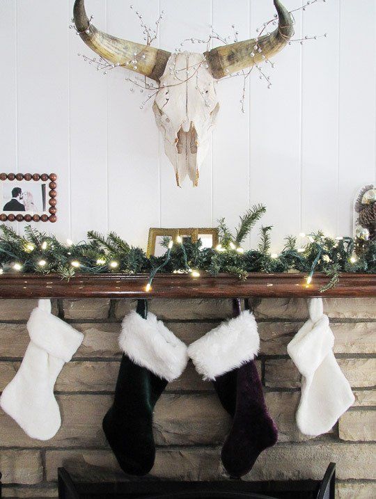 an evergreen garland with lights and some faux fur stockings hanging on the mantel