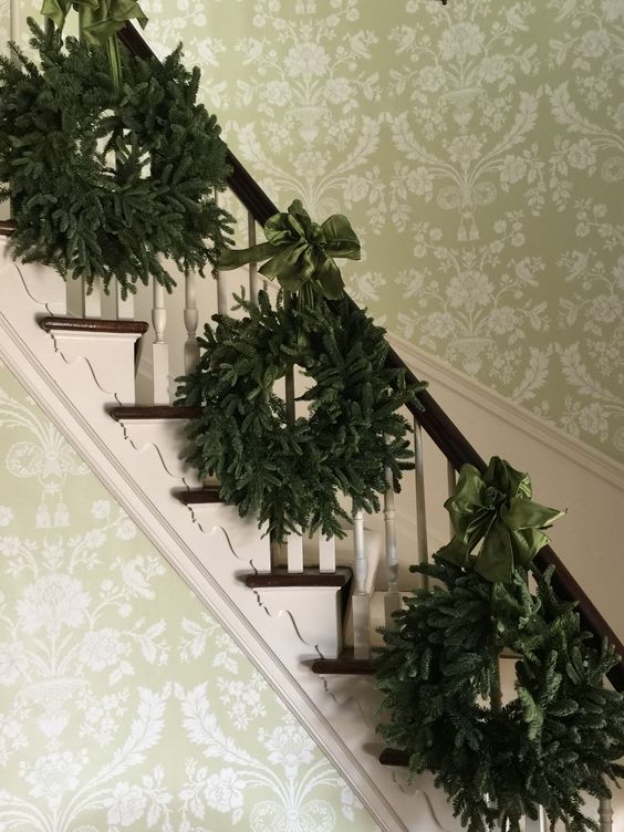 a trio of evergreen wreaths with emerald ribbon bows for decorating stairs