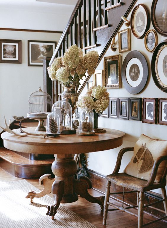 a large rustic wooden pedestal table with a fall display and a galery wall on the stairs