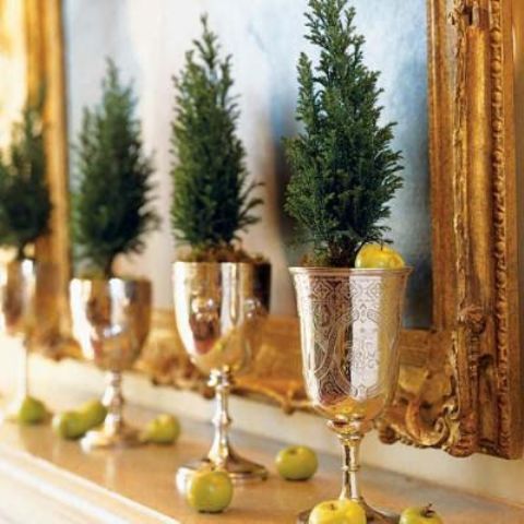 a mantel display with little evergreen trees in gold goblets and small apples
