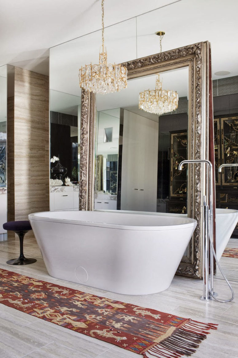 a mirror wall, an additional vintage mirror next to it and a glam chandelier over the bathtub