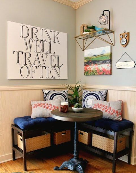 a small and cozy breakfast nook with a round table and an upholstered bench with storage crates