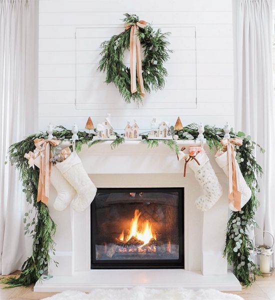 an evergreen wreath and garland, neutral ribbons and a snowy village display on the mantel
