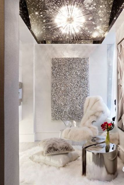 a shiny silver stool or table, a faux fur rug and blanket and a shiny artwork on the wall