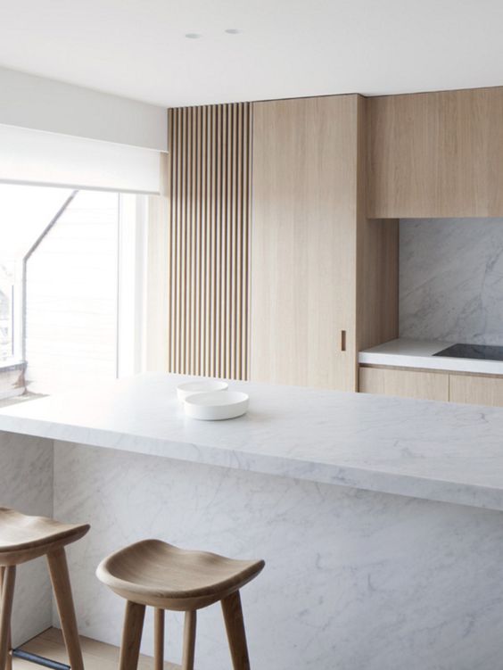 a minimalist kitchen is done with light-colored wood and marble to make it more interesting