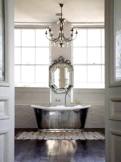 a shiny silver free-standing bathtub, a matching vintage mirror and a crystal chandelier