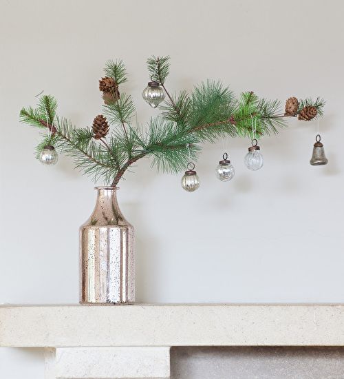 a pine branch with pinecones and some vintage ornaments in a single stem vase