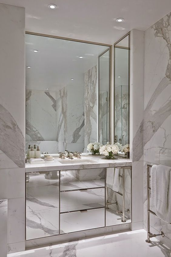 Light colored marble and a built in mirrored vanity and mirrors on three sides