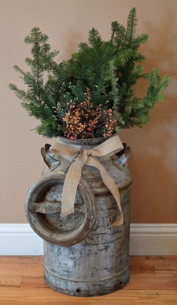 a vintage milk churn with a burlap bow, evergreen branches and berries for outdoor decor