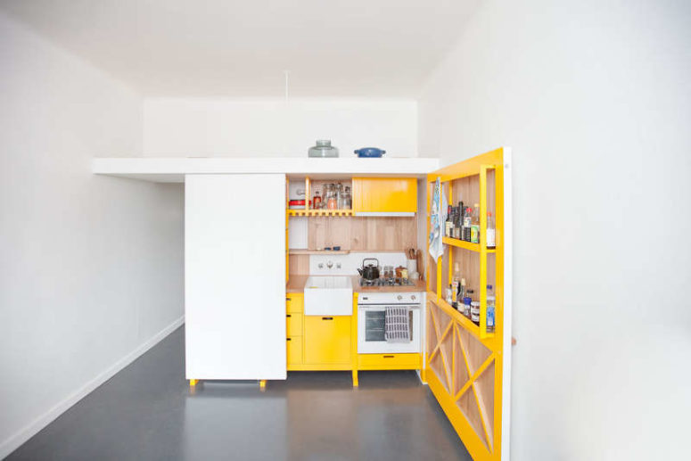 This chic mini kitchen was built for a studio apartment and features bold yellow cabinets and lots of storage space