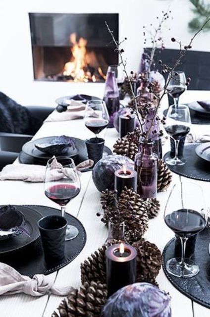 a black and purple New Year's table setting with oversized pinecones, purple candles and black chargers and plates