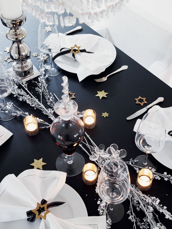 a black table decorated with gold stars, candles, silver branches and candles