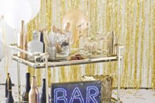 09 a brass bar cart with white and gold balloons, black and gold bottles and a neon sign