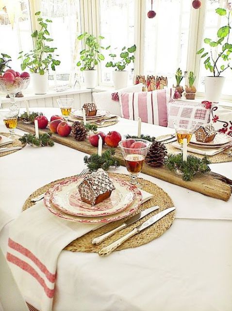 a cozy rustic tablescape with gingerbread house cookies, evergreens, pinecones, apples and candles