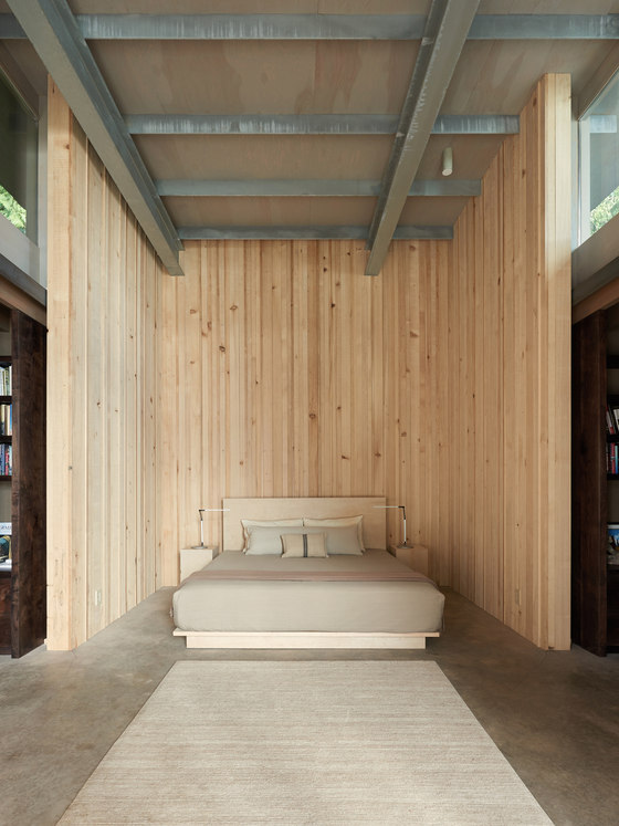 The guest bedroom is clad with natural wood and there's an upholstered creamy bed