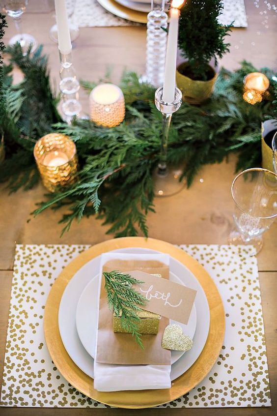 a modern glam tablescape with a gold sequin placemat, evergreens, gold mercury glass candle holders and glitter touches