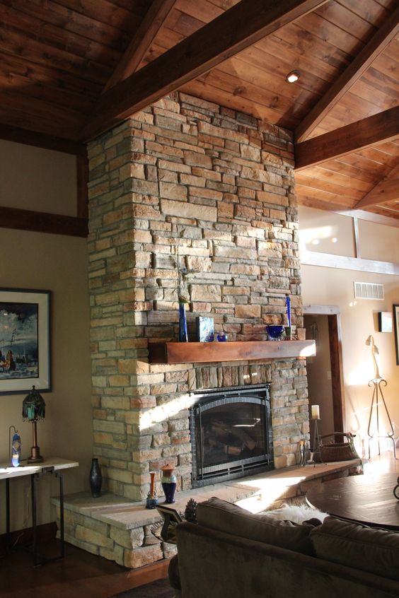 a rustic stone clad fireplace with a wooden mantel surrounded with candles