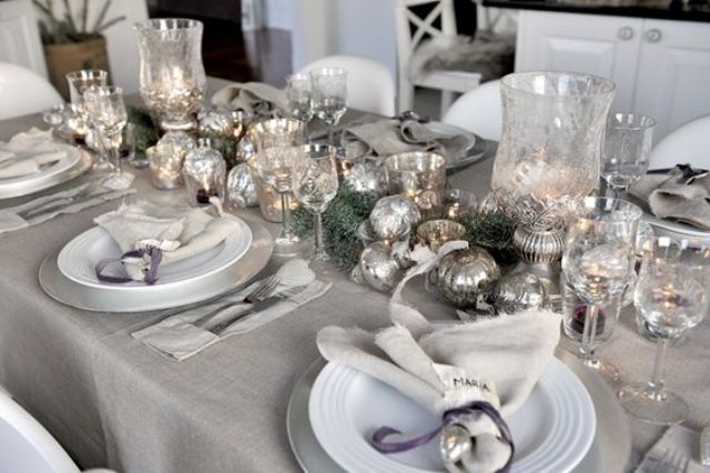 a silver grey tablescape with ornaments, glasses, jingle bells and silver chargers looks frosty and romantic