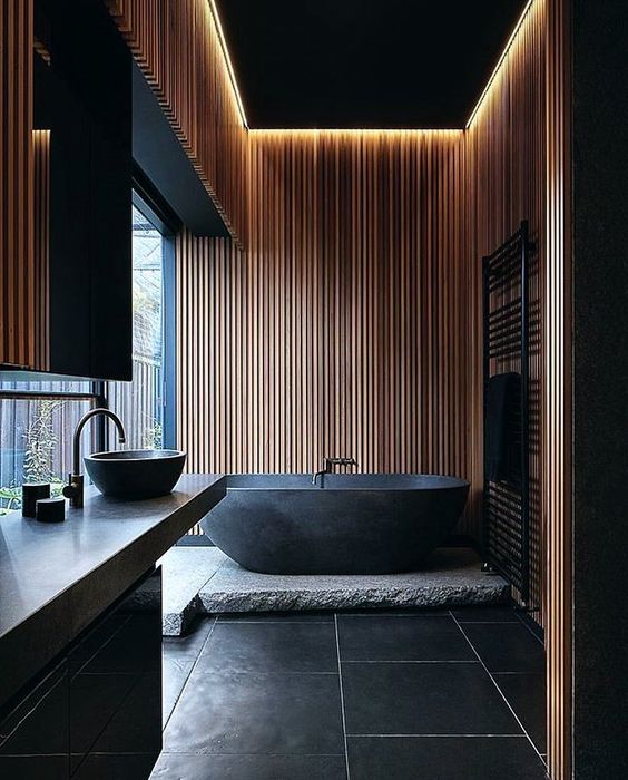 A Japandi bathroom with black and light colored wood is highlighted with a natural stone slab and countertop